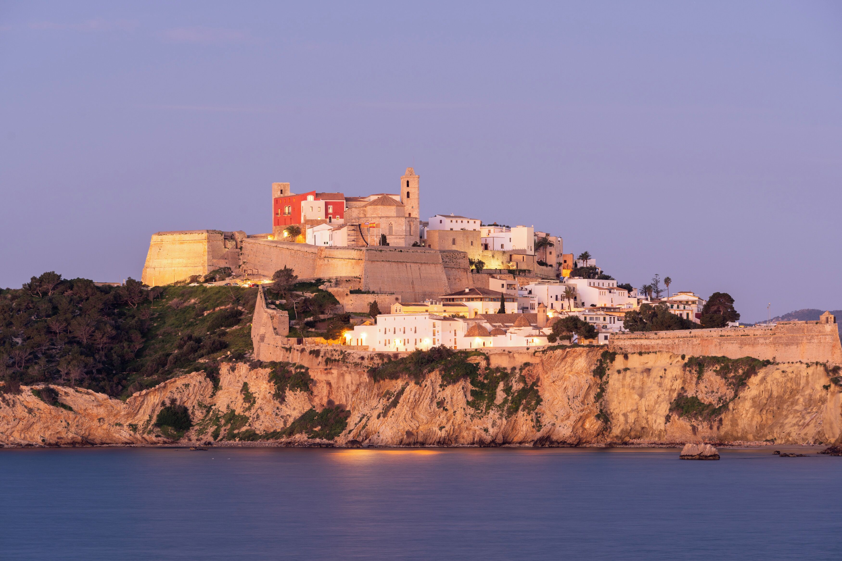 A coastal town with historic buildings, a prominent tower, and a fortified wall.