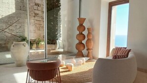 Una sala de estar moderna con una mesa de vidrio, un sillón redondo y un sofá. Hay jarrones grandes y una planta en maceta.