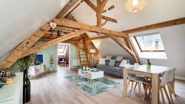 Habitación estilo loft con vigas de madera a la vista, comedor con mesa y sillas, un sofá y vistas a través de un tragaluz.