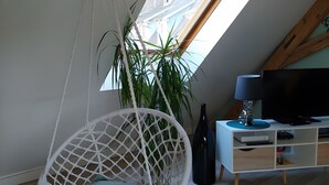 Una habitación con techo inclinado, una silla colgante, un escritorio con televisor y un ventanal grande.