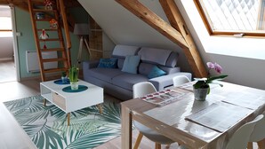 Una habitación estilo loft con techo inclinado, un sofá, una mesa de comedor y una escalera.