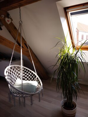 Quarto com cadeira suspensa, planta em vaso, vigas de madeira e janela com vista.