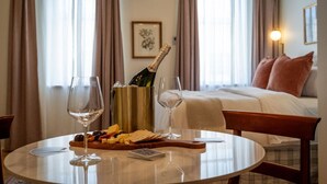 Una habitación de hotel con una cama, una mesita de noche con una botella de champán, copas y una tabla de quesos.