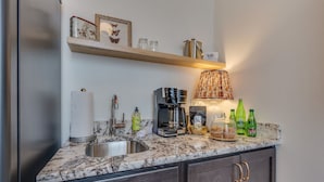 A kitchen with a marble countertop, a coffee maker, a kettle, and various bottles. - The Downtown Post The Gracie Suite (Elizabethton)