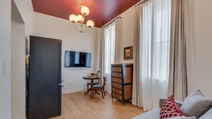 A modern living room with a grey sofa, a wooden sideboard, a dining area with a table and chairs, a flat-screen TV mounted on the wall, and a chandelier. - The Downtown Post The Gracie Suite (Elizabethton)