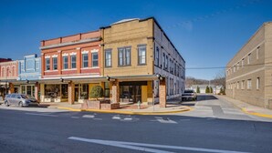 A street view with a row of multi-story buildings, including a hotel with a covered entrance and a parking lot. - The Downtown Post The Gracie Suite (Elizabethton)