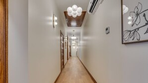 A hallway with wooden flooring, wall-mounted lights, and a ceiling light fixture. - The Downtown Post The Gracie Suite (Elizabethton)