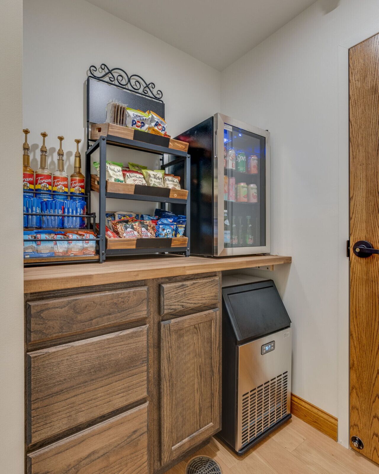 A kitchenette with a refrigerator, a shelf with snacks, and a trash bin.