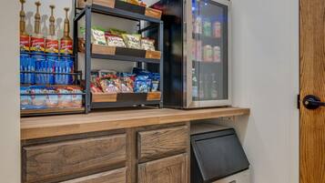 A kitchenette with a refrigerator, a shelf with snacks, and a trash bin.