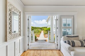 A room with a wooden floor, a white couch, and a view of a garden through an open door. - Gulffront WaterColor Condo w/ 6-Seat LSV (Santa Rosa Beach)
