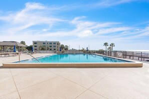 A rectangular pool with a tiled deck, surrounded by a metal fence, and a building with multiple balconies in the background. - Mansions By The Sea 306a - Premier (Treasure Island)