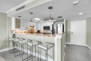 A modern kitchen with white cabinets, a granite countertop, stainless steel appliances, and bar stools. - Mansions By The Sea 306a - Premier (Treasure Island)