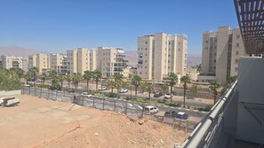 A residential area with multi-story buildings, a road with vehicles, and palm trees. - Desert View Home • Private Balcony by SeaNRent (Eilat)