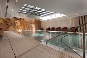 An indoor swimming pool with a glass barrier, a stone wall, and a skylight. - Desert View Home • Private Balcony by SeaNRent (Eilat)