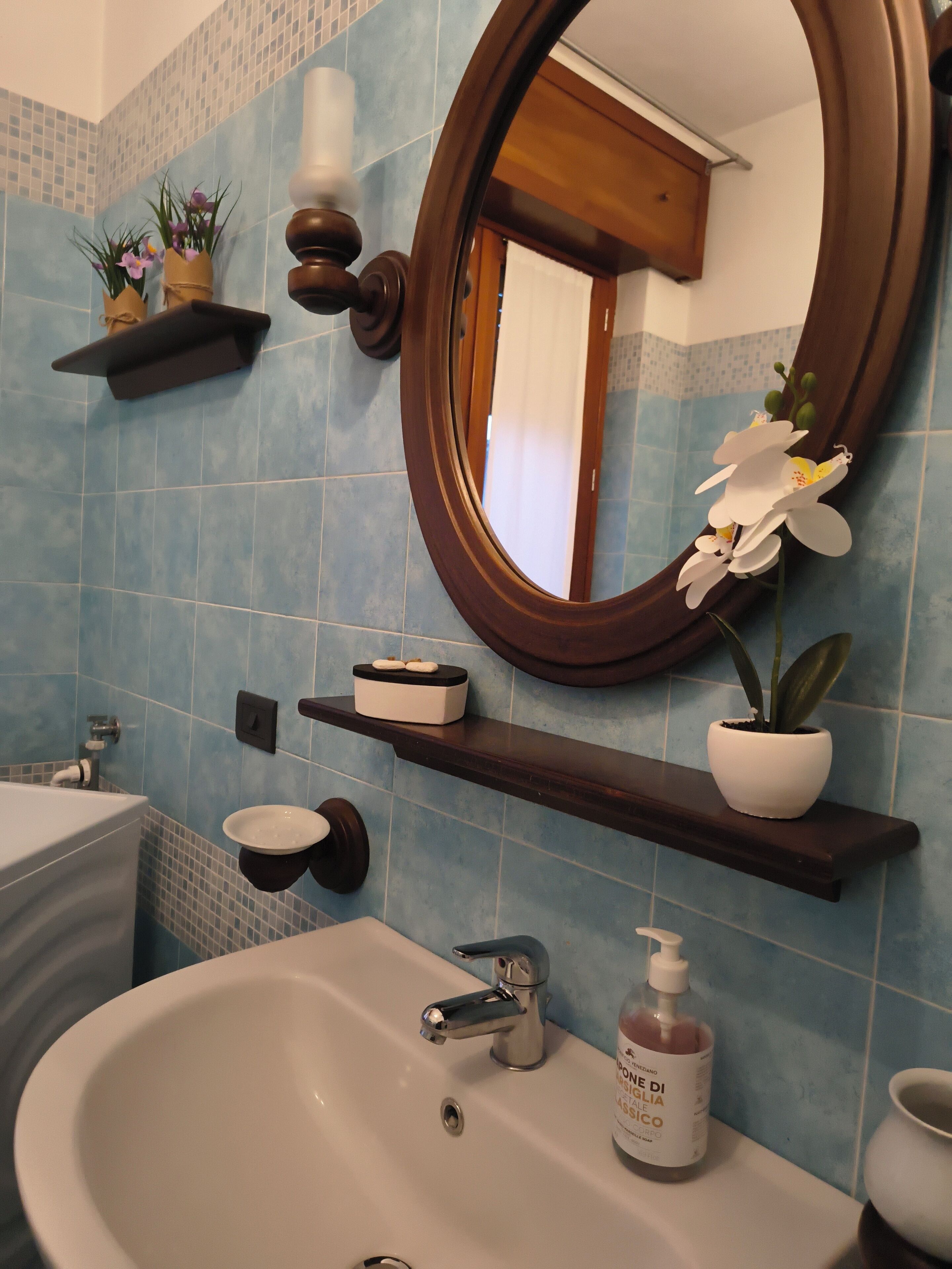 Ein Badezimmer mit einem weißen Waschbecken, einem Spiegel und einem Regal mit einer Topfpflanze.