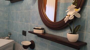 Ein Badezimmer mit einem weißen Waschbecken, einem Spiegel und einem Regal mit einer Topfpflanze.
