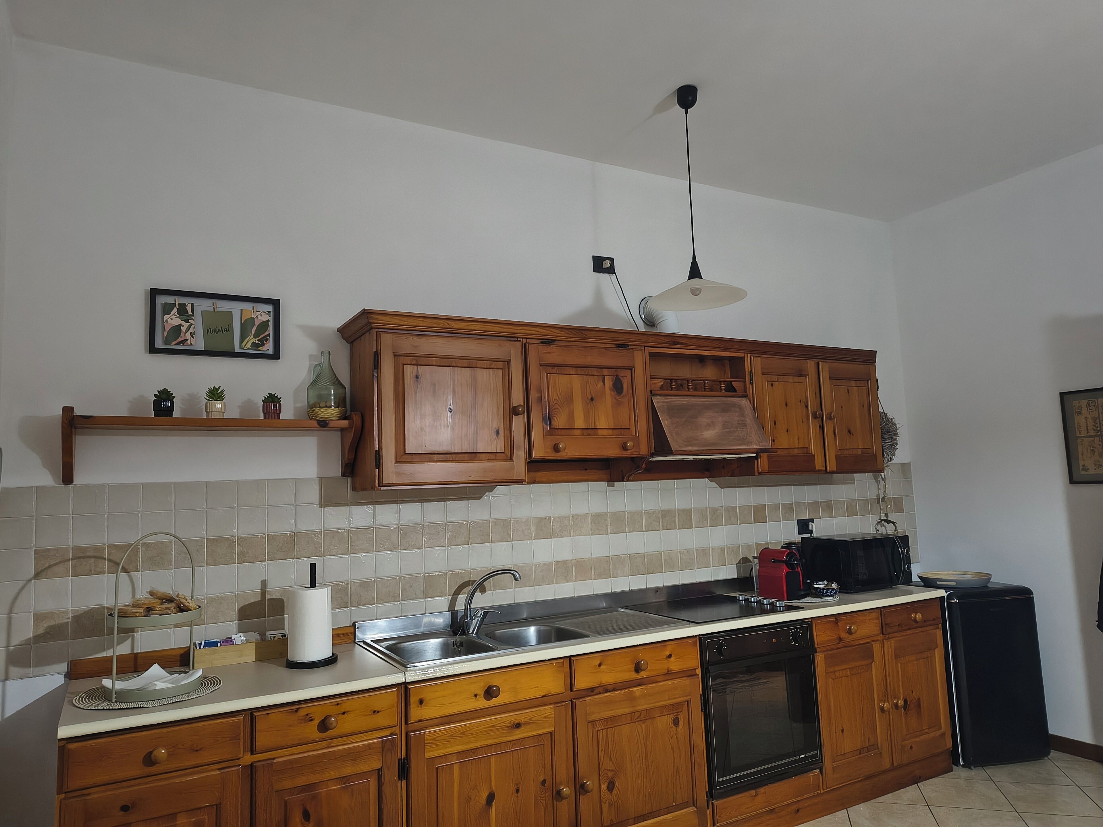 A kitchen with wooden cabinets, a stainless steel sink, a black oven, and a small refrigerator.