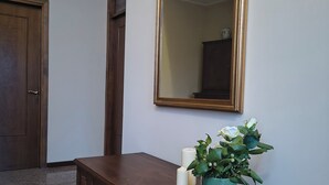 Une commode en bois avec un miroir et une plante en pot, placée dans un couloir.