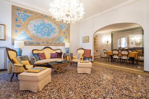 A spacious living room with a large, ornate chandelier, a patterned wall tapestry, and a dining area with yellow tablecloths. - Ca' Lipoli - Four Bedroom Apartment, Sleeps 6 (Venice)