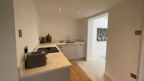 A modern kitchen with white cabinets, a marble countertop, and a built-in oven. - Samphire House (Cromer)