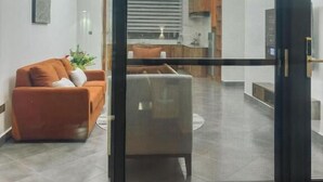 A modern living room with a sofa and a coffee table, a kitchen in the background, and a sliding glass door leading to the living area. - Valonia Apartments  (Arusha)