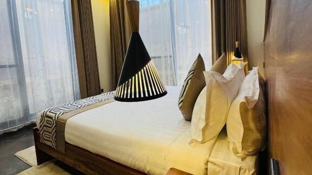 A modern hotel room with a large bed, a wooden nightstand, and a bedside table with a phone. - Valonia Apartments  (Arusha)