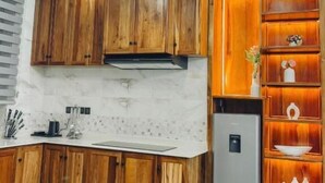 A modern kitchen with wooden cabinets, a marble backsplash, and a built-in wooden shelf unit with decorative items. - Valonia Apartments  (Arusha)