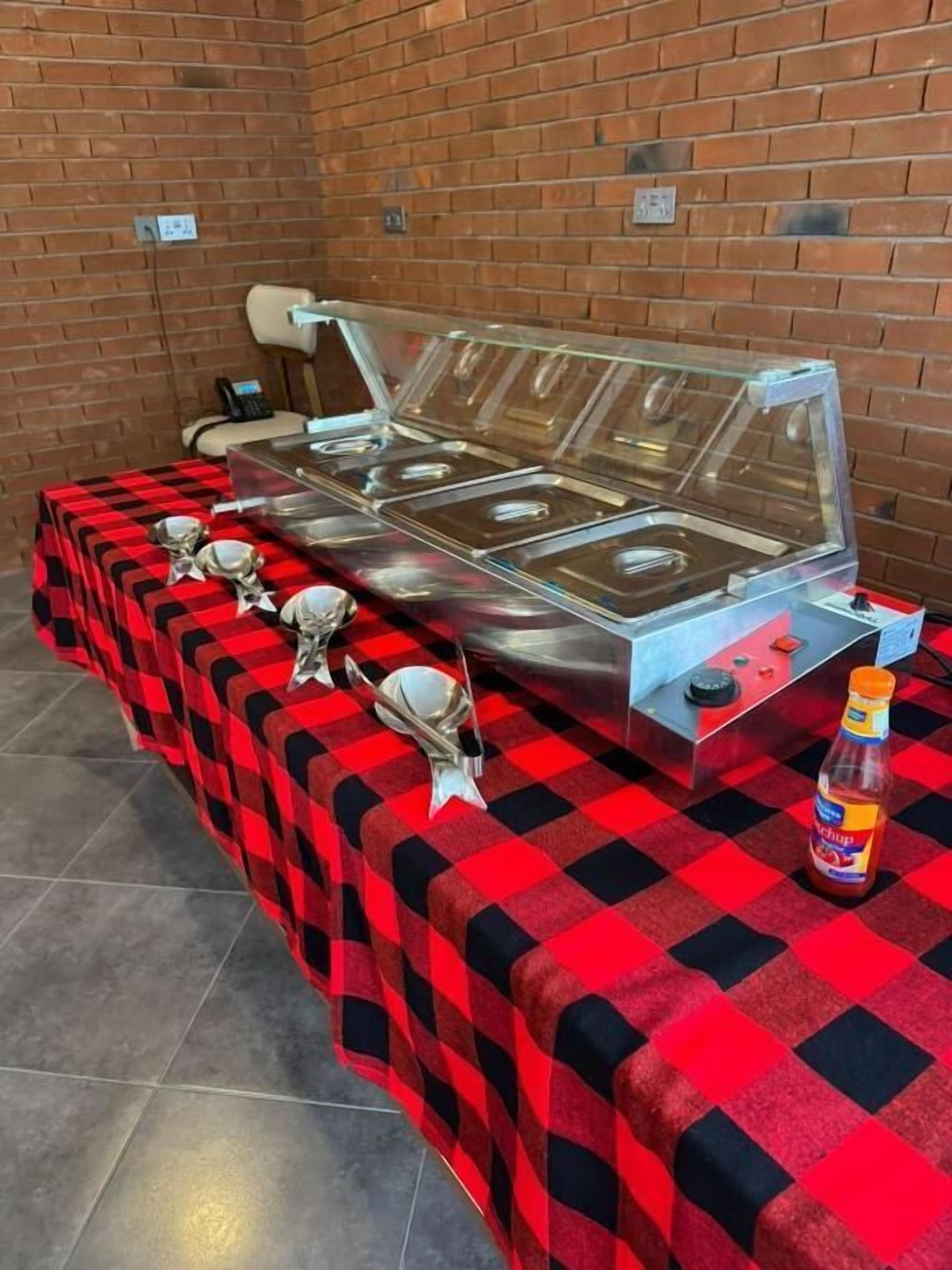 A buffet setup with multiple serving stations, a check-in counter, and a bottle of ketchup on a checkered tablecloth.
