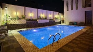 A swimming pool with a checkered border, surrounded by a tiled deck and a white building with multiple windows. - Valonia Apartments  (Arusha)