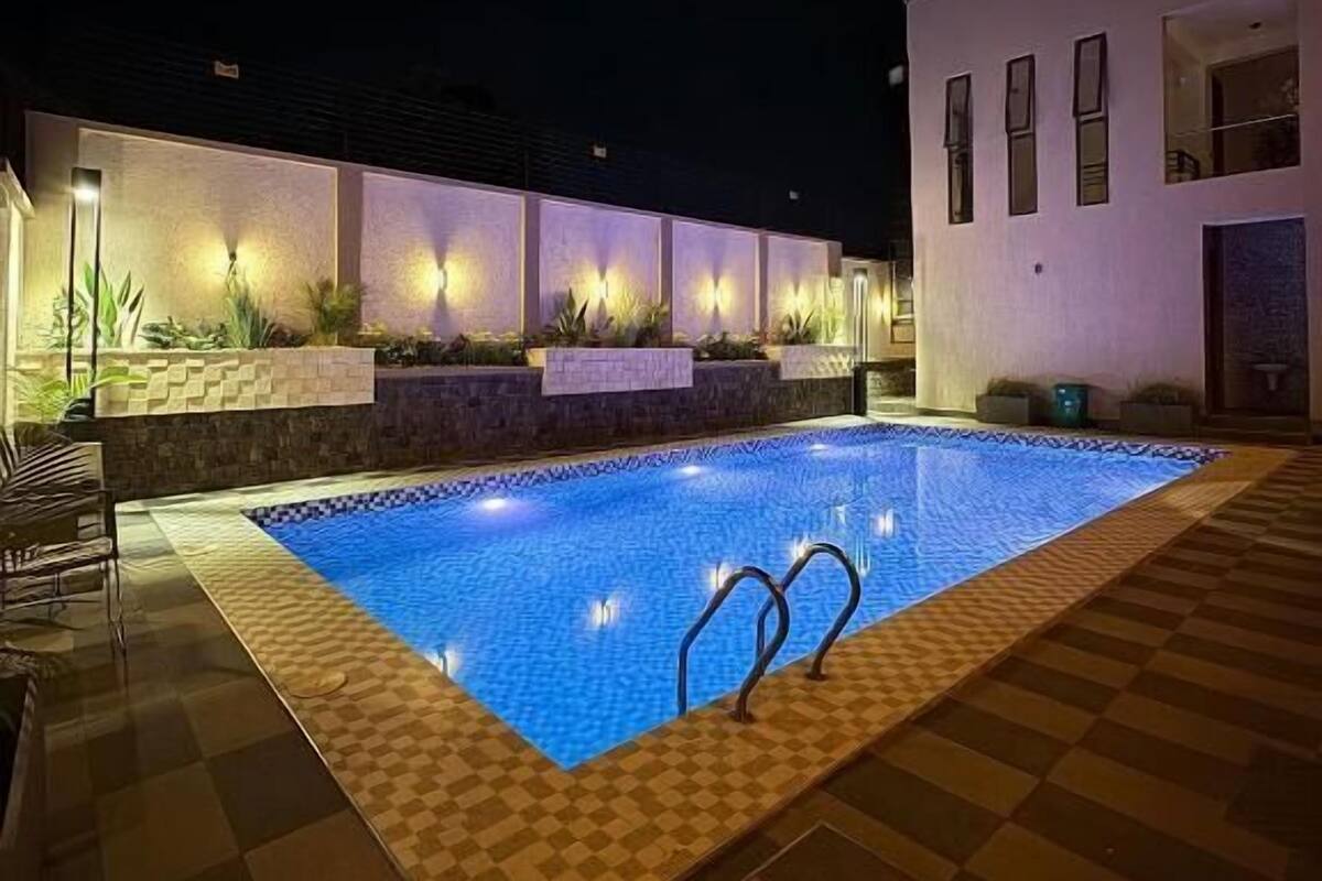 A swimming pool with a checkered border, surrounded by a tiled deck and a white building with multiple windows.