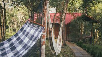 A hammock tied to a tree in a wooded area with a rustic cabin in the background.