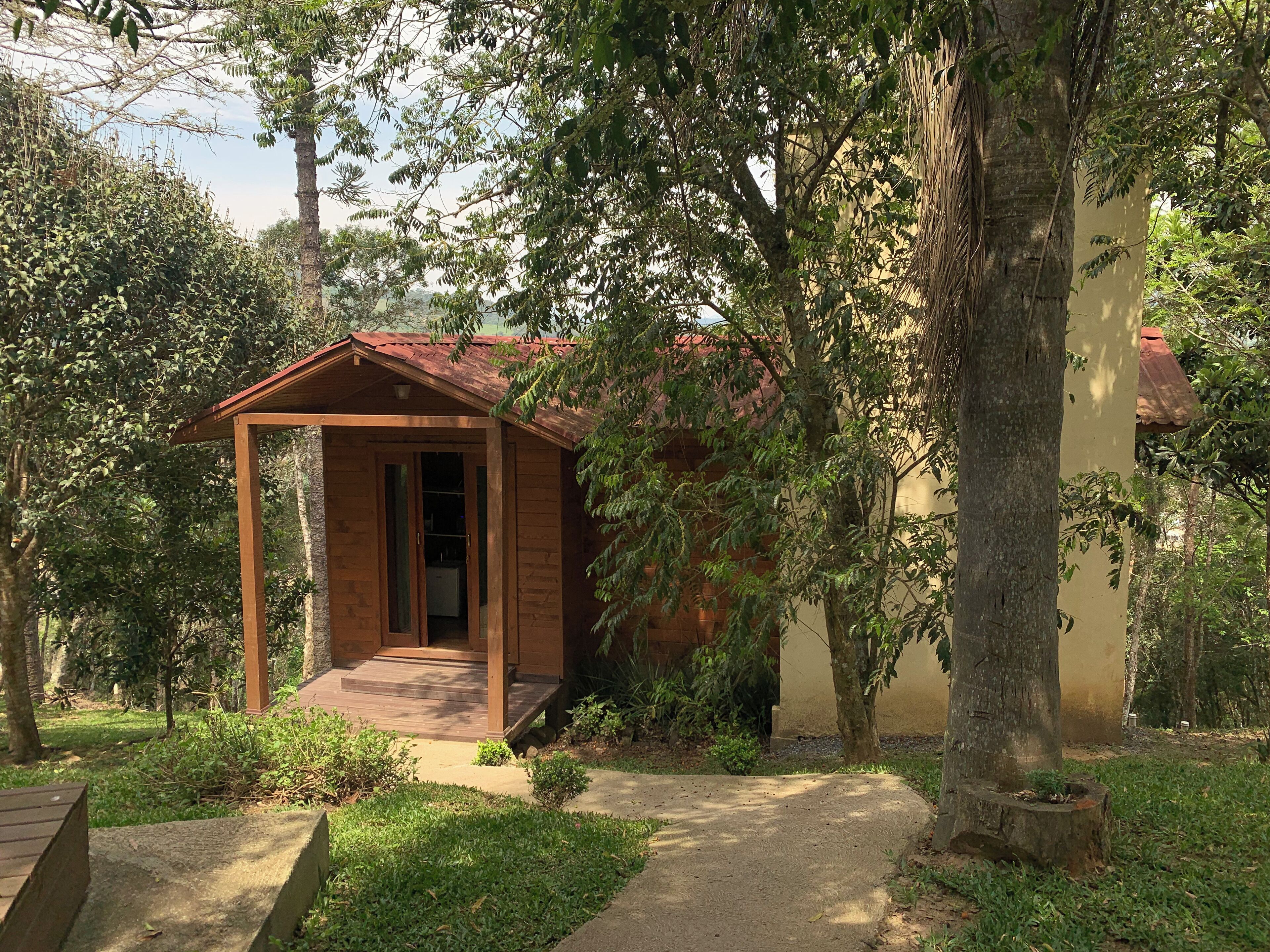 Una pequeña cabaña de madera con techo rojo, rodeada de exuberante follaje y árboles.