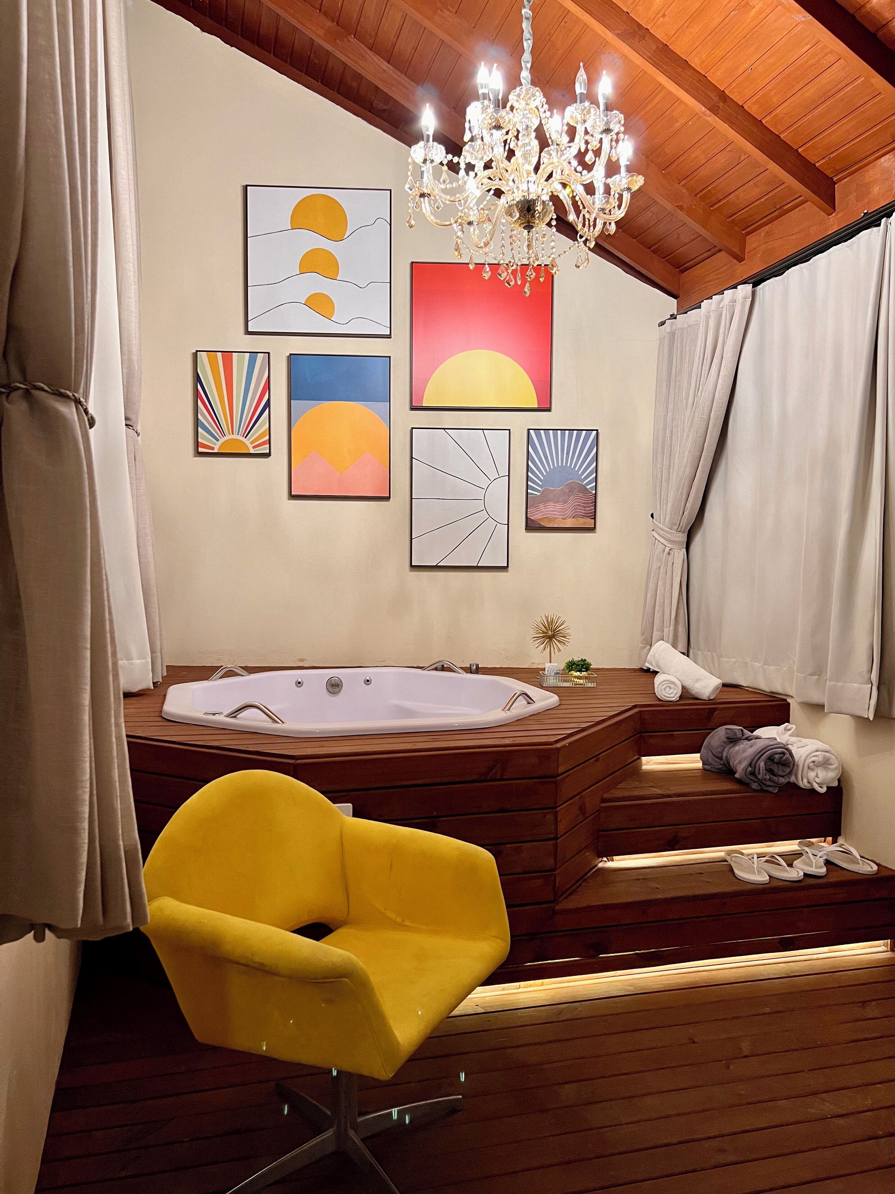 Un baño moderno con una bañera de madera, una silla amarilla y obras de arte en la pared.