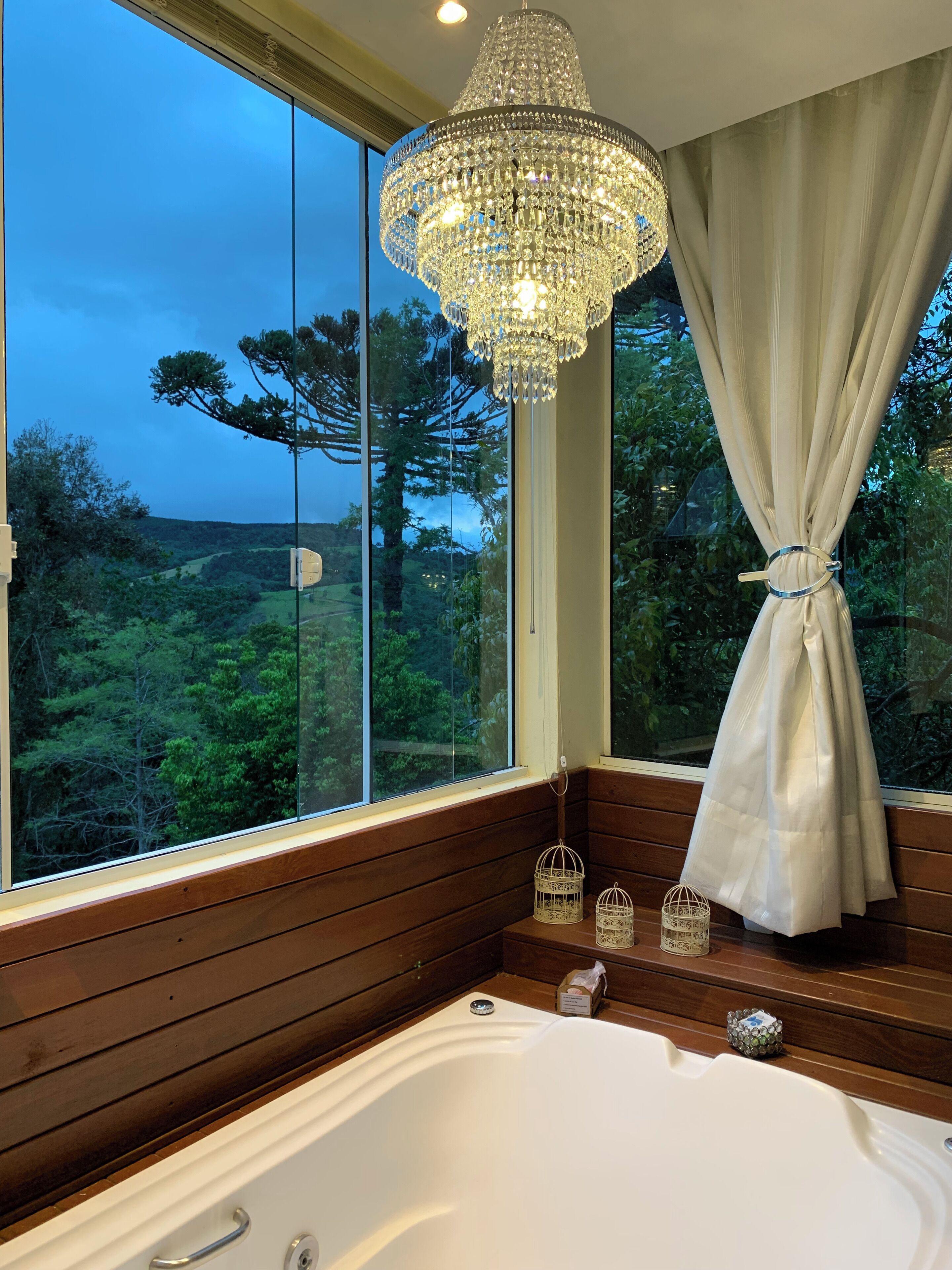 A bathroom with a large bathtub, a chandelier, and a view of the outdoors.