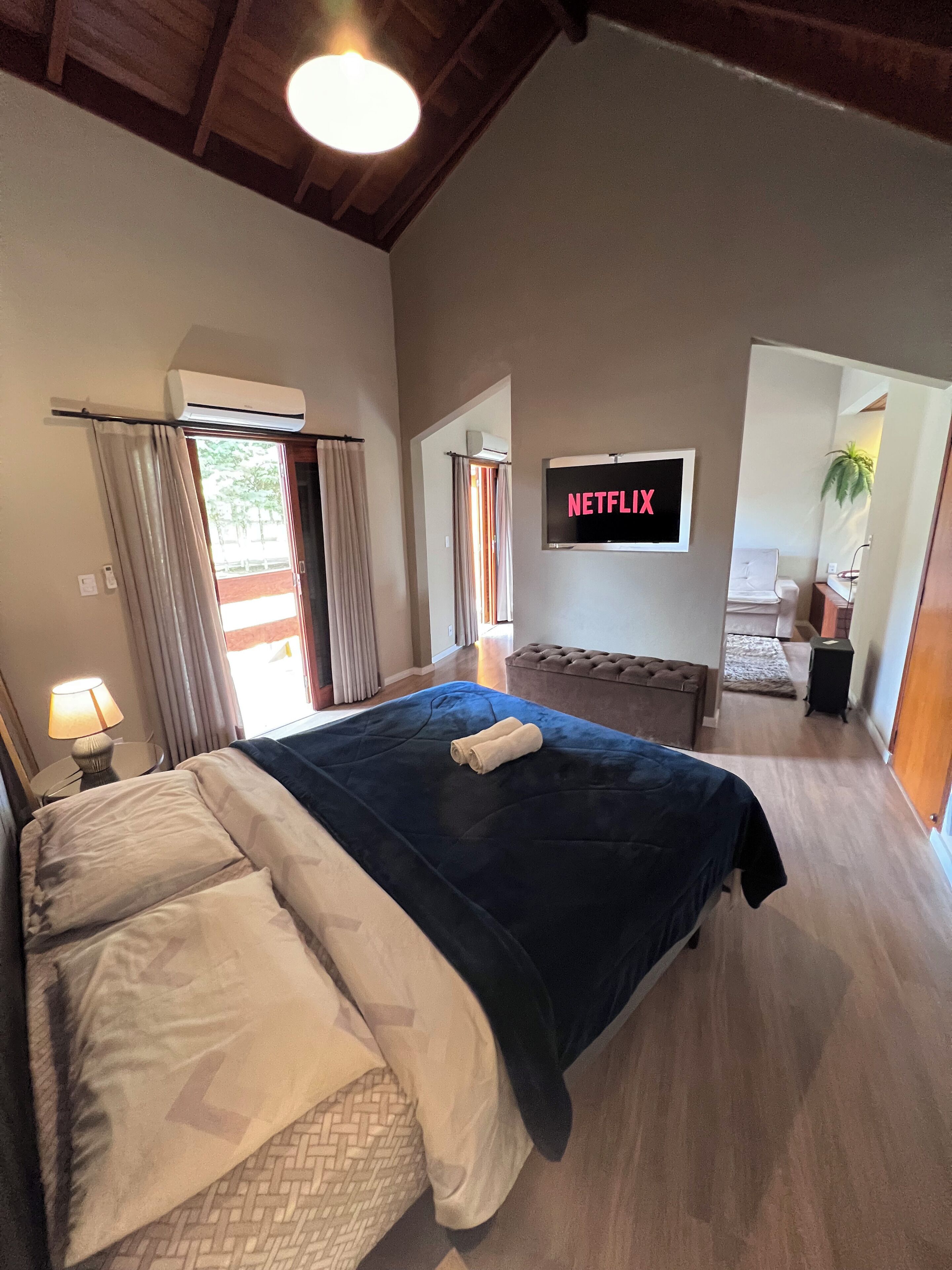 Ein Schlafzimmer mit einem großen Bett, einer Klimaanlage, einem Fernseher und Blick ins Freie.