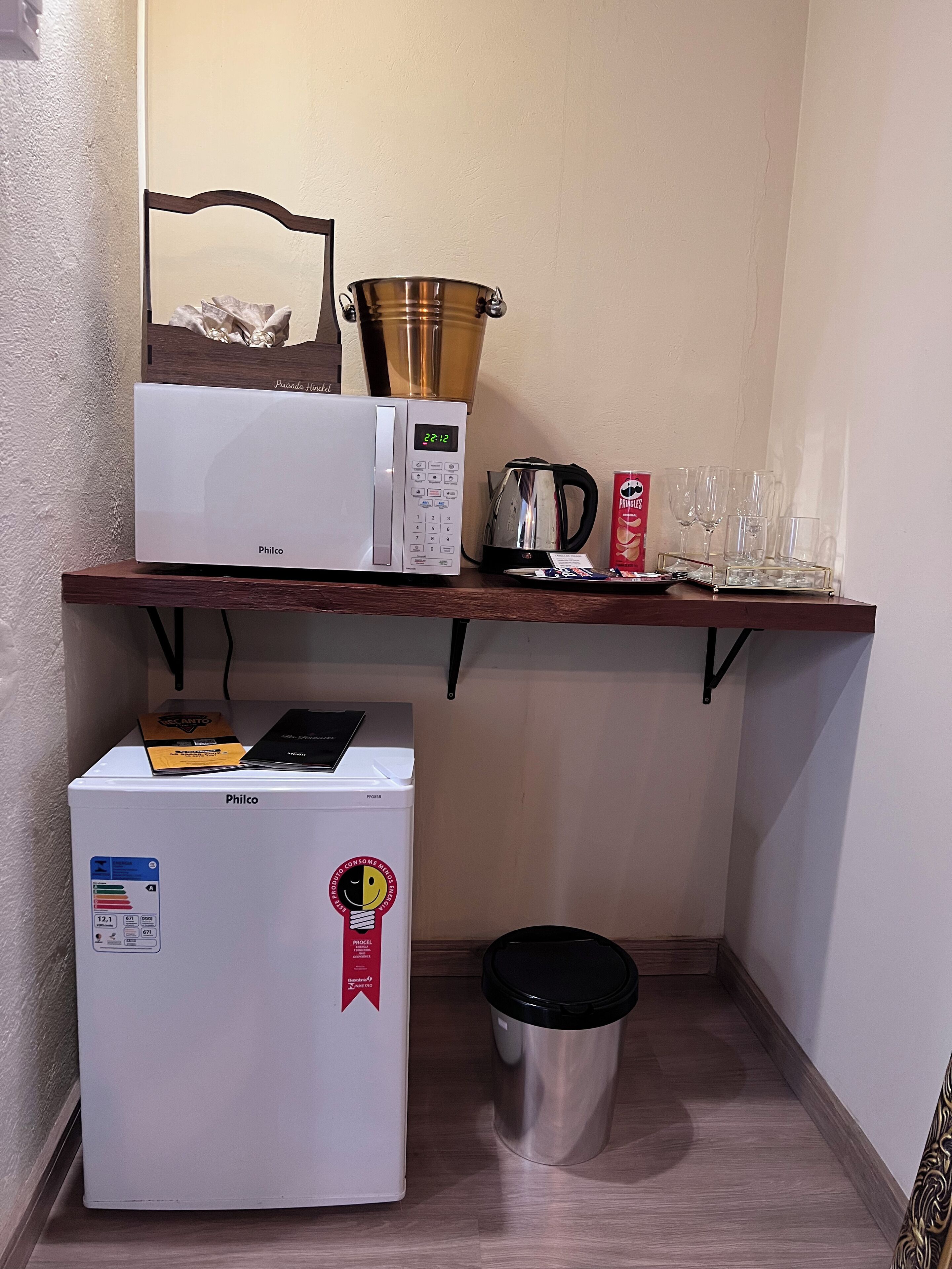 Eine kleine Küchenzeile mit einer Mikrowelle, einem kleinen Kühlschrank, einem Wasserkocher und einem Mülleimer.