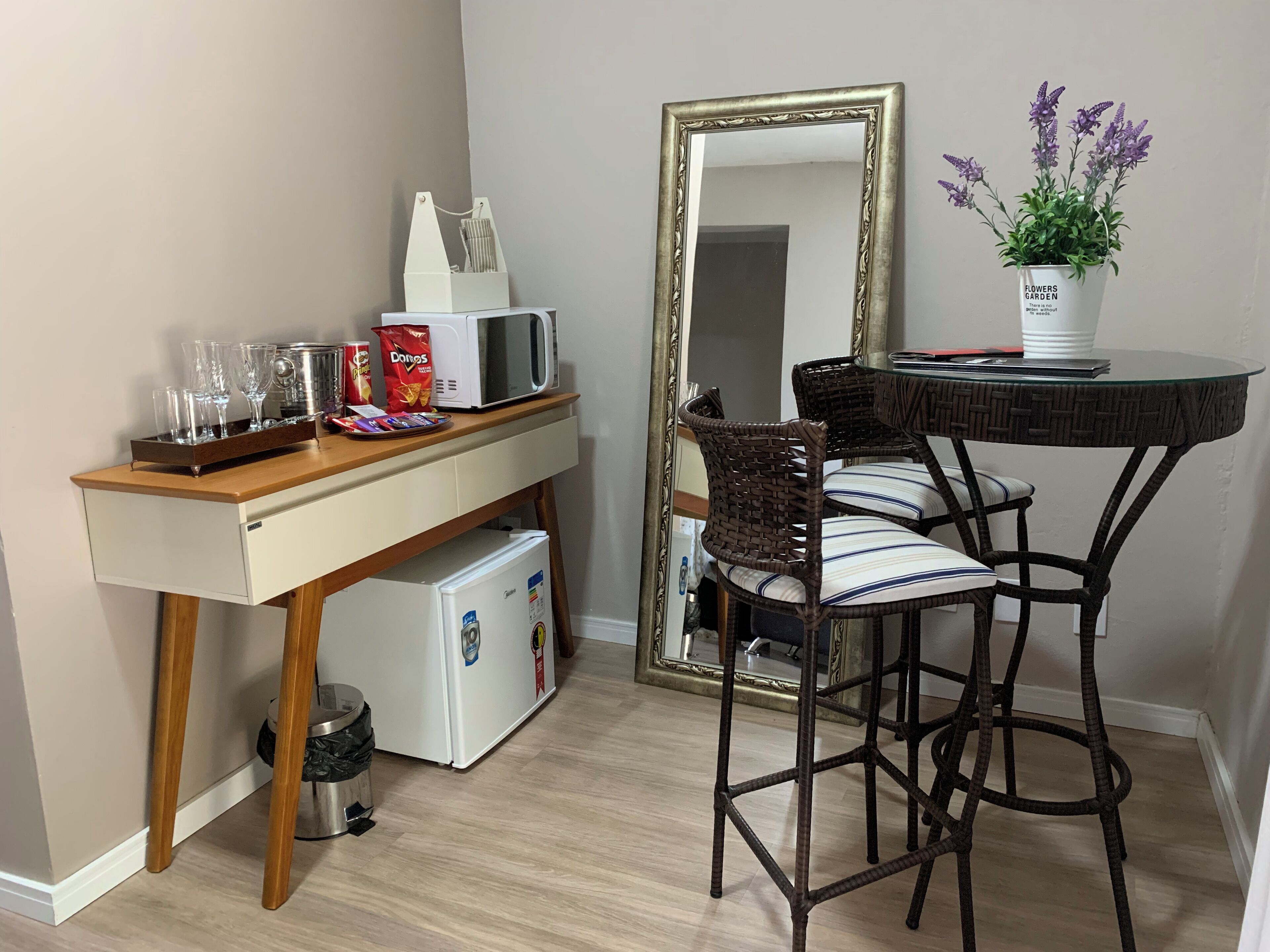 A compact kitchenette with a microwave, toaster, and small refrigerator. There is a dining area with a table and two chairs, and a large mirror on the wall.