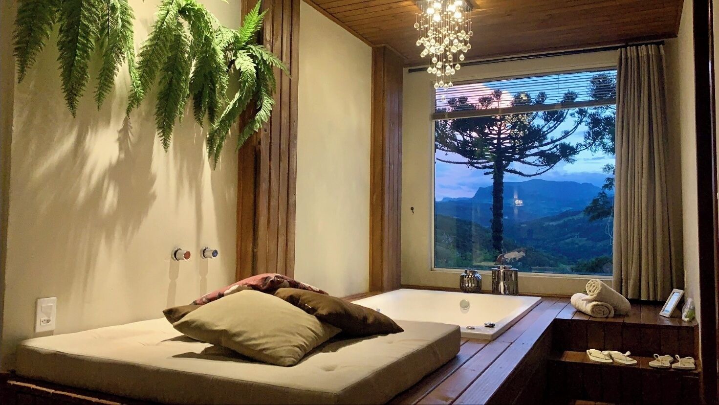 A bedroom with a large window, a bathtub, and a bed with pillows.