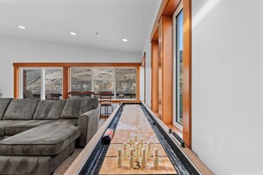 A modern living room with a foosball table, a sectional sofa, and large windows offering a view of the outdoors.