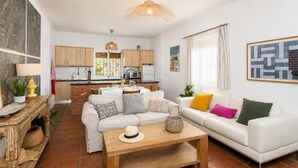 Un salon moderne avec un canapé blanc, une table basse en bois et une cuisine en arrière-plan.