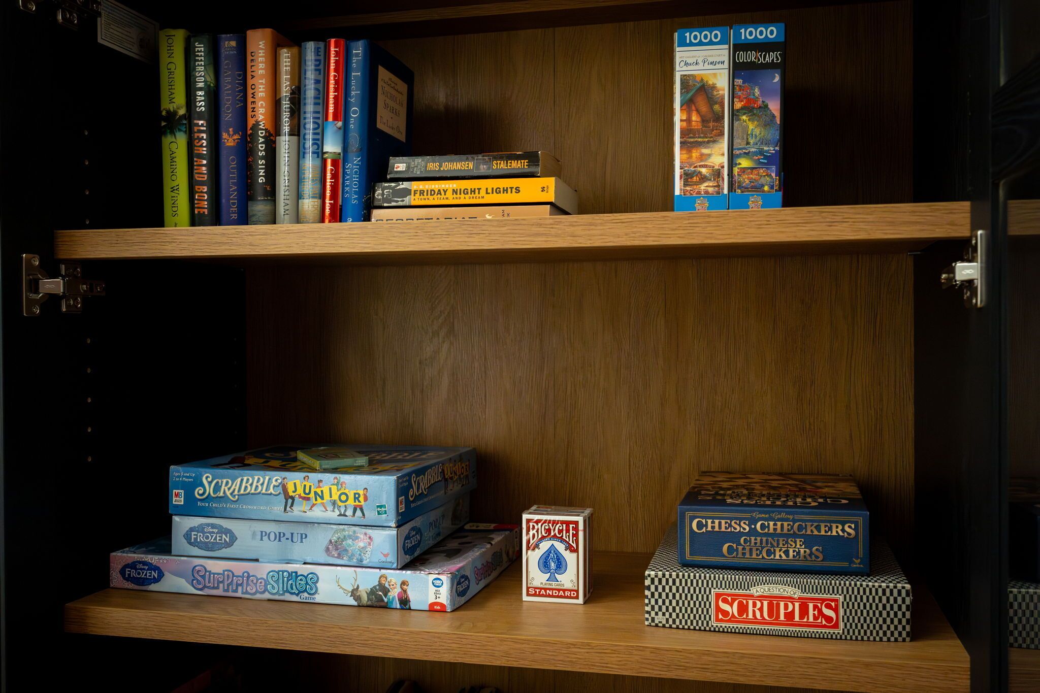 Une étagère contenant divers jeux de société et casse-têtes, notamment Scrabble, La Reine des neiges et le jeu de dames.
