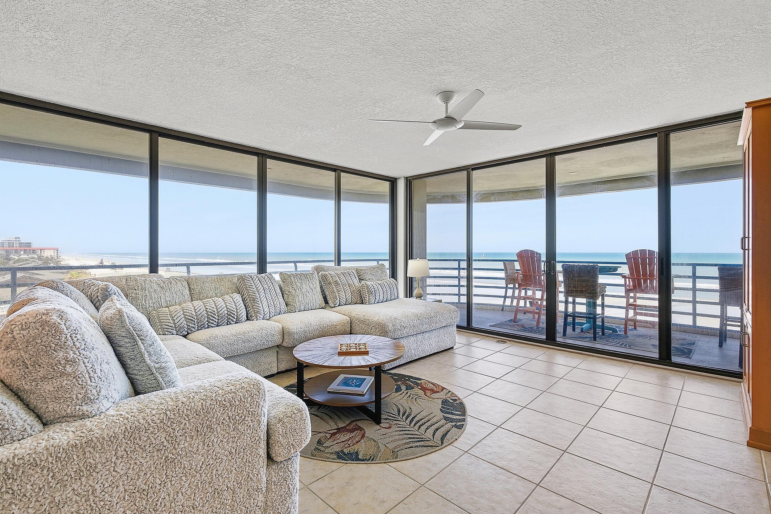 A spacious living area with a large sectional sofa, a round coffee table, and a ceiling fan.