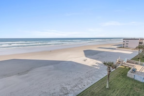 A beach view with a building in the foreground, a clear sky, and a calm sea. - Ebb Tide 407 (New Smyrna Beach)