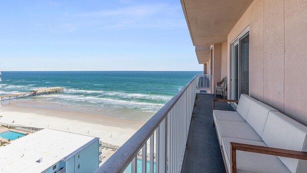 A balcony with a view of the beach and ocean, a pool, and a white sofa. - Salida del Sol 1101 (Daytona Beach Shores)