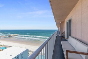 Un balcón con vista a la playa y al océano, una piscina y un sofá blanco.