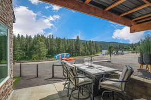 An outdoor patio with a table and chairs, overlooking a forested area and a body of water. - Waterfront home w/River access & Amazing views (Post Falls)