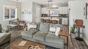 A modern living room with a grey sofa, wooden coffee table, and a dining area with a white table and chairs. - Waterfront home w/River access & Amazing views (Post Falls)