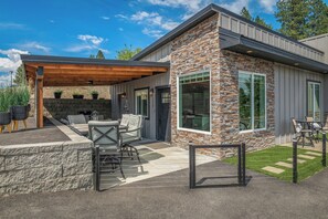 A modern house with a stone exterior, a covered patio with outdoor furniture, and a well-maintained lawn. - Waterfront home w/River access & Amazing views (Post Falls)