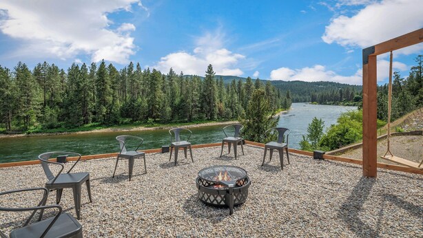 A terrace with a fire pit, outdoor seating, and a view of a river and forest. - Waterfront home w/River access & Amazing views (Post Falls)