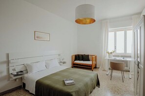 Ein Schlafzimmer mit Bett, Nachttisch, Lampe, Stuhl und einem Fenster mit Vorhängen.